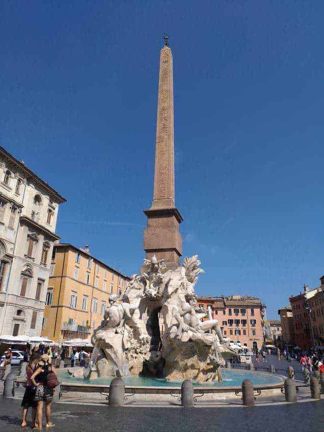 Colonna dell'Obelisco e fontana in Piazza Navona, Roma, Italia, con sculture barocche e edificio storico sullo sfondo.