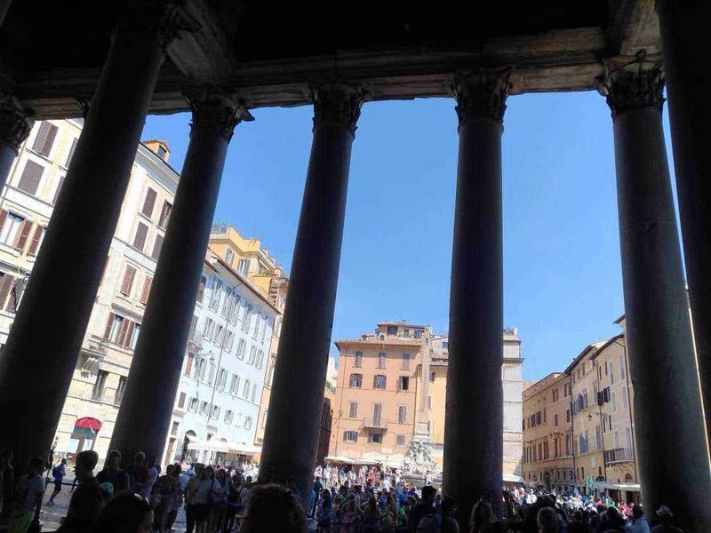 Piazza Navona a Roma in stile barocco 8 Immagine di un antico foro romano con colonne di granito, illuminato dal sole, affollato di visitatori, con palazzi storici italiani sullo sfondo, rappresenta il cuore della città di Roma.