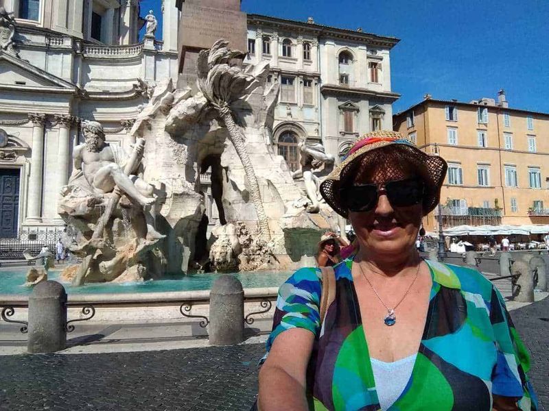 Piazza Navona a Roma in stile barocco 5 Fonte: Fontana dei Quattro Fiumi a Piazza Navona, Roma, con donna sorridente con cappello e occhiali scuri in primo piano.