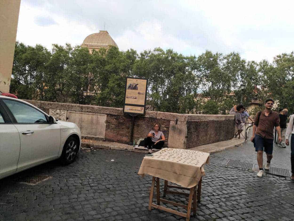 Variante 1: Albero e ponte di pietra con passanti e auto, atmosfera urbana serale, decay di strada, elementi di vita quotidiana, contesto storico, stile fotografico urbano, insegne e natura.