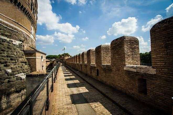 Mura storiche di Roma con camminamento e parapetto in ferro, sotto un cielo azzurro con nuvole bianche, emerge l'antica sicurezza e bellezza della città eterna.
