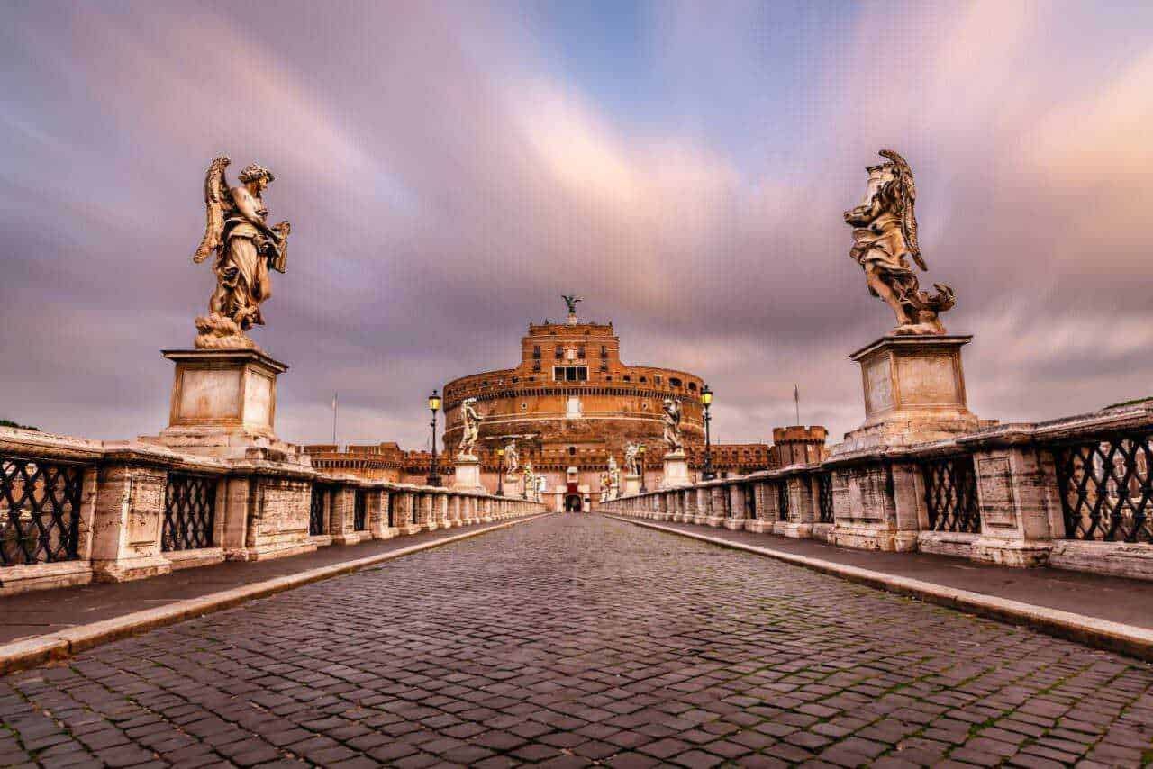 Antico ponte sul Tevere che conduce al Castel Sant'Angelo a Roma, con sculture barocche e cielo al tramonto, perfetto per appunti di viaggio e post sul blog incentrati sulla storia della Capitale.