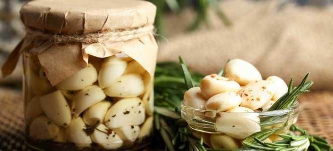 Alimento sottaceto di aglio fresco in barattolo e in ciotola con erbe aromatiche, ideale per ricette gourmet e antipasti salutari.