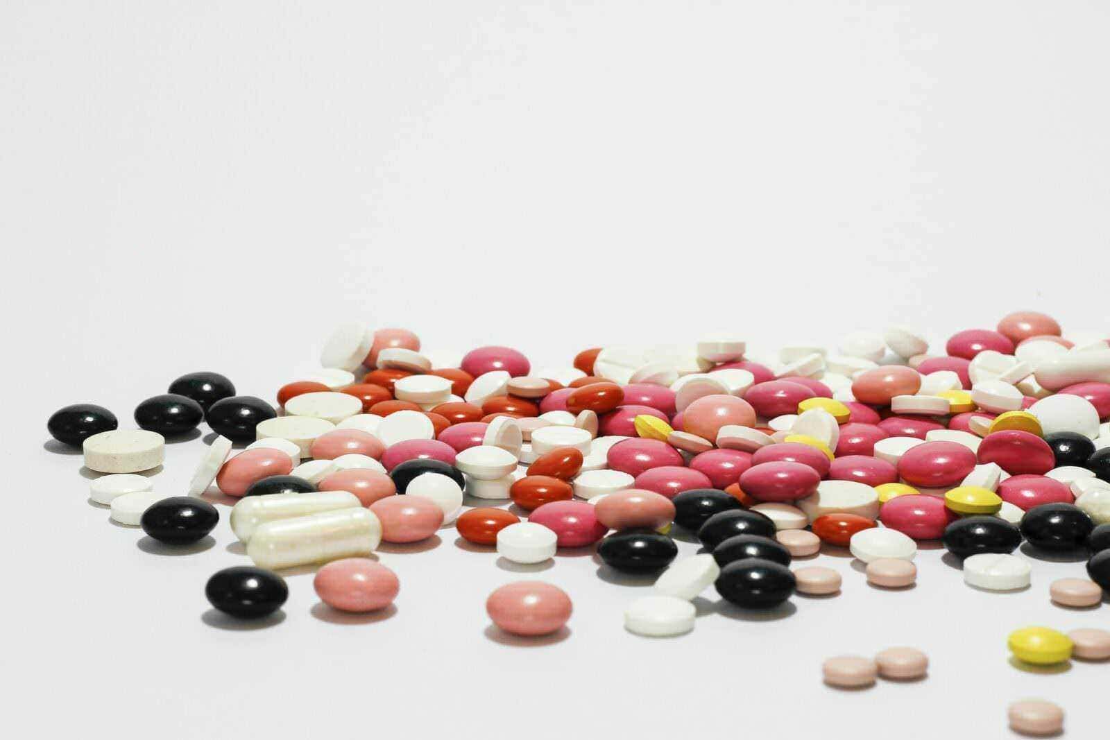 Come agiscono sui batteri: Pillole di diversi colori e forme sparse su uno sfondo bianco, rappresentano medicinali, integratori o farmaci. Ideale per articoli su salute, farmaci, medicina o benessere. Immagine simbolica di farmaceutica e trattamento medico.