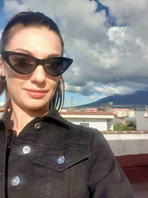 Come vestirsi bene con outfit sportivo ma elegante 6 Sophisticated woman with sunglasses taking selfie outdoors on a bright day in Italy.