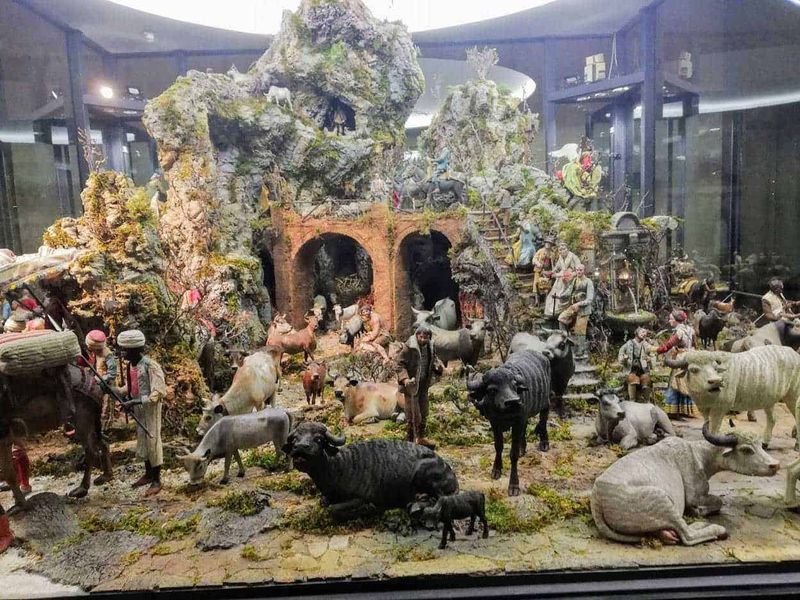 Cosa vedere Reggia di Caserta, location Star Wars 13 Rilievo di presepe con figure di animali e persone in stile tradizionale, ambientato in un paesaggio montano con archi in mattoni, piante verdi e figurine artigianali, rappresentazione natalizia dettagliata e ricca di atmosfera.