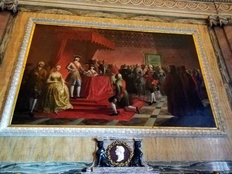 Cosa vedere Reggia di Caserta, location Star Wars 9 Raffigura un dipinto storico con figure in abiti d'epoca in un luminoso salone, decorato con cornici dorate e dettagli artistici eleganti, che rappresenta un momento di grande importanza storica o culturale in un museo.