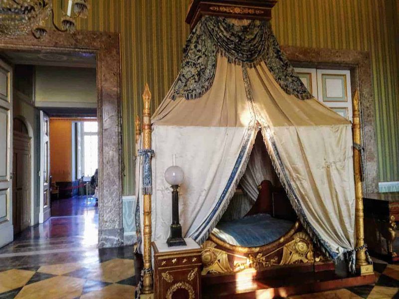 Cosa vedere Reggia di Caserta, location Star Wars 10 Antico letto a baldacchino in stile barocco in una stanza storica, decorato con drappeggi e dettagli dorati, all'interno di un palazzo d'epoca con pareti rivestite in velluto e pavimento in parquet.