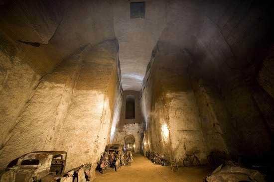 Un grande bunker sotterraneo abbandonato con pareti di cemento e biciclette parcheggiate, illuminato da luci calde, che mostra un’architettura unica e suggestiva.