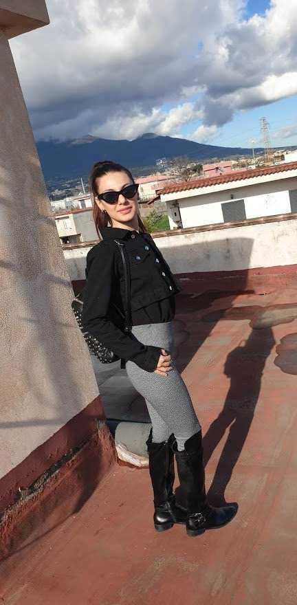Ragazza alla moda in abbigliamento autunnale con stivali neri e occhiali da sole su un terrazzo con vista sui tetti e montagne sullo sfondo, atmosfera urbana e rilassata, lifestyle e moda.