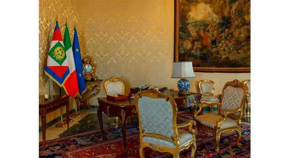 Bandiere italiana e europea in ufficio governativo con arredamento elegante e storico.
