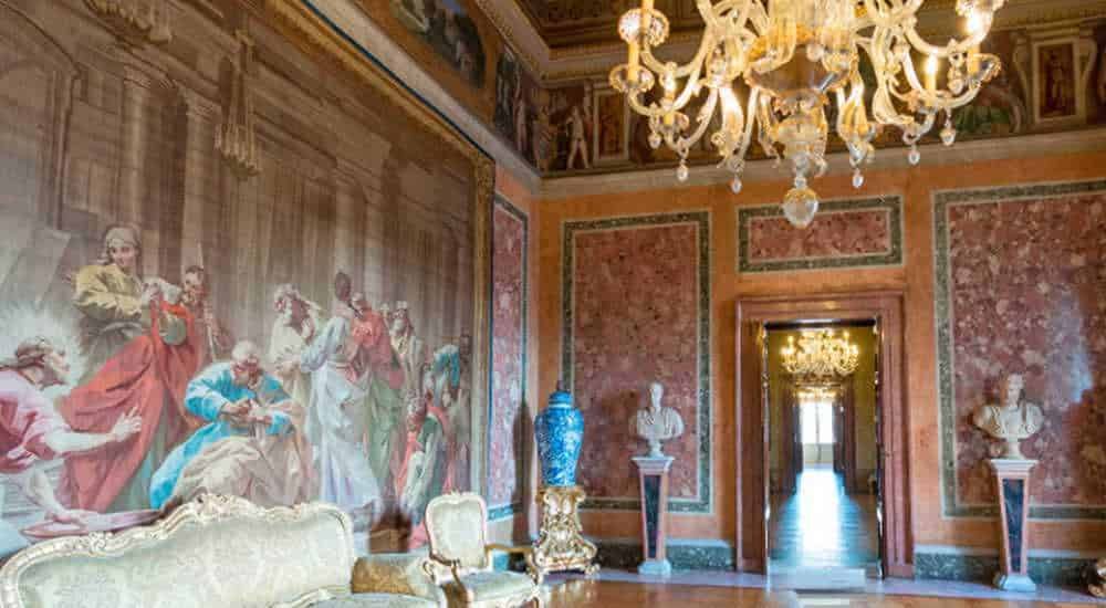 Elegante salone con affreschi classici, lampadario chandelier in stile barocco, arredi antichi e statue di marmo, ambienti storici ricchi di decorazioni d'arte e cultura.