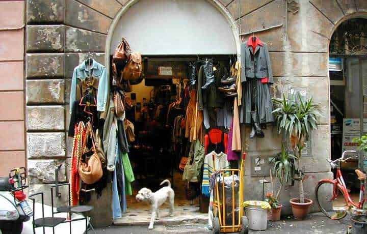 Vestiti e accessori vintage in un negozio in strada, con uno sfondo di edificio storico. Abbigliamento usato, moda sostenibile, negozio di abbigliamento di seconda mano, mercatino vintage, shopping ecologico.