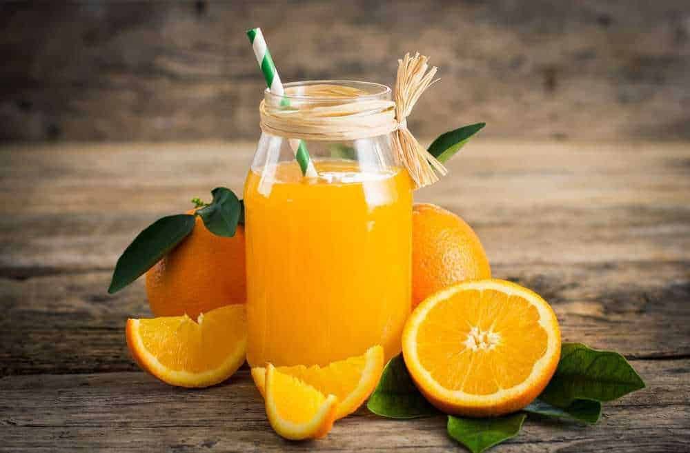 Succo di arancia naturale in un barattolo di vetro con cannuccia verde, accompagnato da arance fresche e foglie verdi, sul tavolo di legno rustico, ideale come esempio di salutare bevanda energetica.