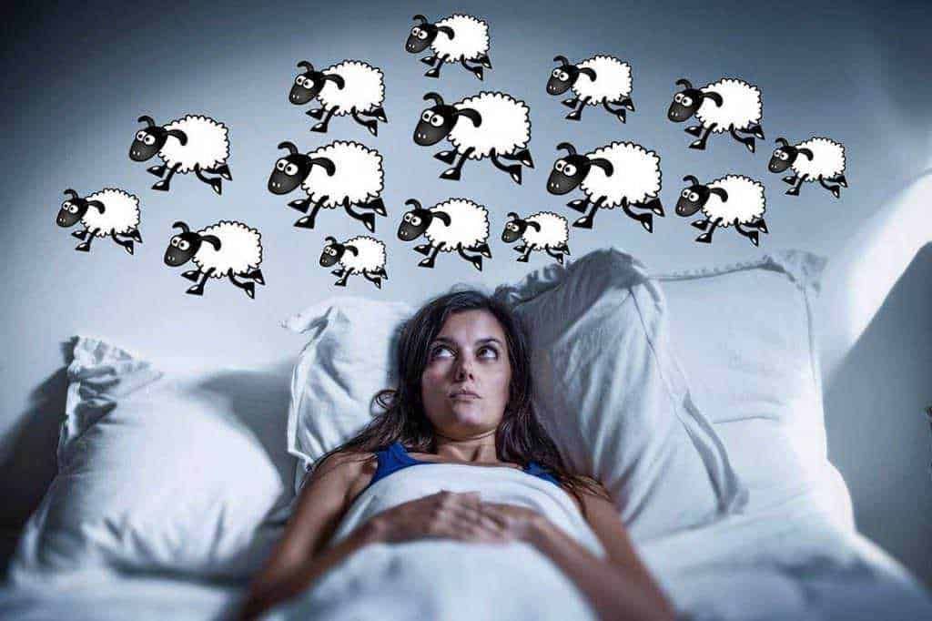 Nuvola di ovini animate sopra una donna sveglia che si trova a letto, simbolo di pensieri o preoccupazioni notturne, rappresentando stress o ansia mentale. Immagine creativa per temi di sogni, pensieri o insonnia.