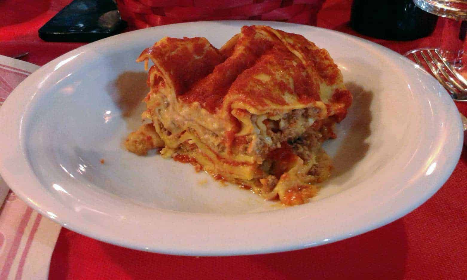 Delicious homemade lasagna with rich tomato sauce, béchamel, and cheese on a white plate, served in a cozy Italian restaurant setting.
