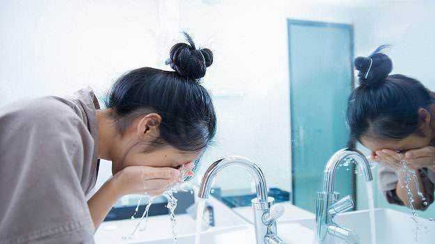 Lavatrice femminile che si lava il viso davanti allo specchio in bagno.