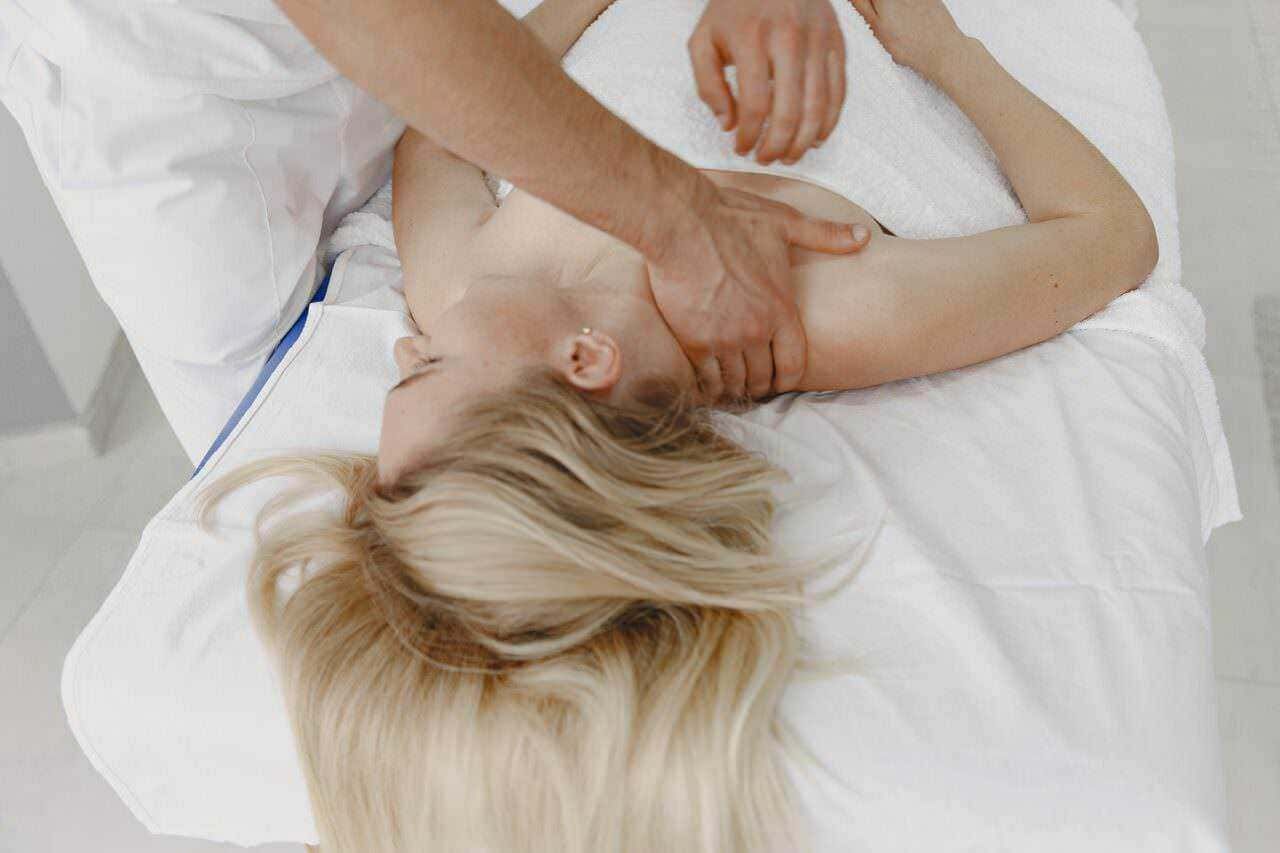 Massaggiatore che compie un massaggio rilassante su una donna sdraiata su un lettino da massaggi, approccio terapeutico e benessere, trattamento decontratturante e relax muscolare.
