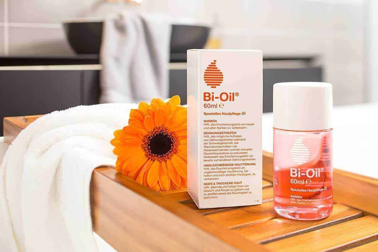 Olio Bi-Oil e unguento per il trattamento delle cicatrici e della pelle screpolata, posizionato su un tavolo di legno con una fiore arancione accanto.