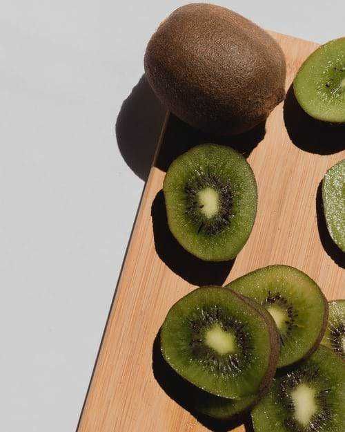 Kiwi benefici: Kiwi interi con polpa verde e semi neri, su un tagliere di legno. Frutta fresca e salutare, ideale per la colazione o uno spuntino energico.