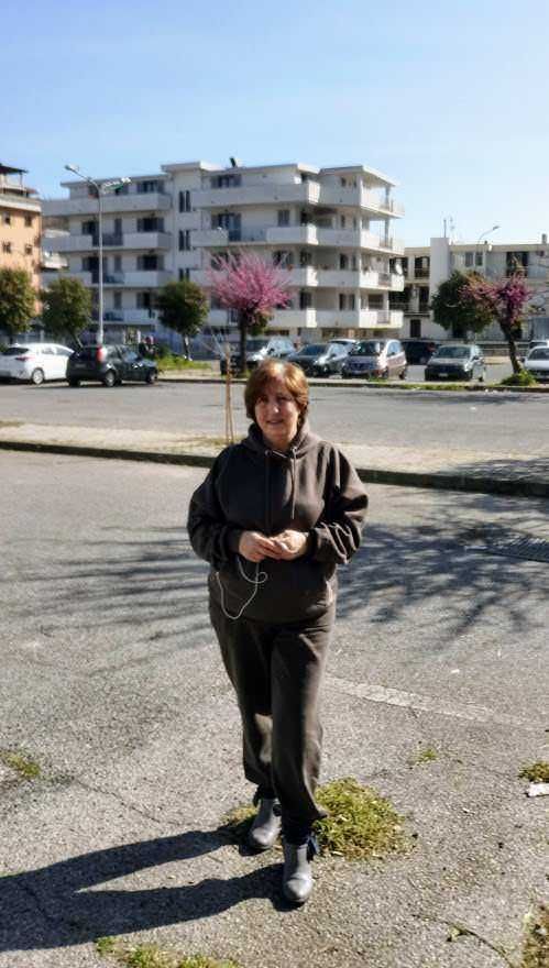 Moda sportiva 2021 per donne piccole e curvy 4 Appunti Sul Blog, donna che cammina nel quartiere urbano con edifici residenziali e alberi in fiore, scenario di vita quotidiana.