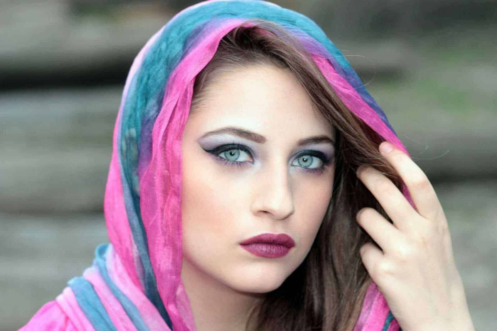 Luxuriosa donna con occhi azzurri, trucco marcato e capelli castani, indossa una sciarpa colorata che avvolge la testa, in un'immagine moda e bellezza.