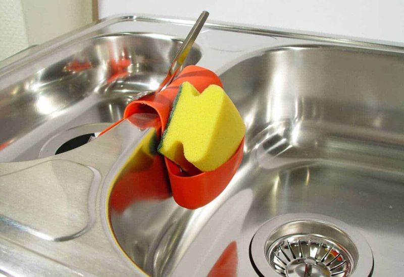 Quale lavello scegliere in cucina, singolo o doppio? 6 Panni da cucina attaccati a un lavello in acciaio inox con spugnetta gialla e detergente rosso.