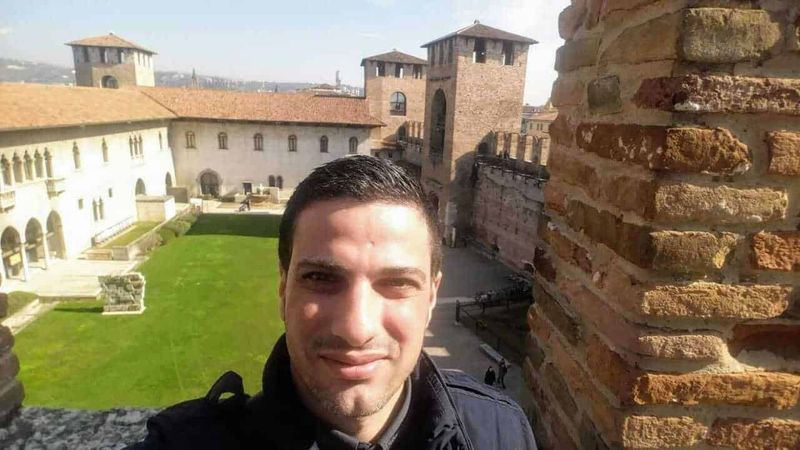 Dove si trova Verona, Meteo e cosa vedere nella Piccola Roma (2026) 10 Faro di un edificio storico con panorama sulla città, uomo in primo piano in un sito turistico, architettura antica, cultura italiana, viaggio in Italia, attrazioni storiche.