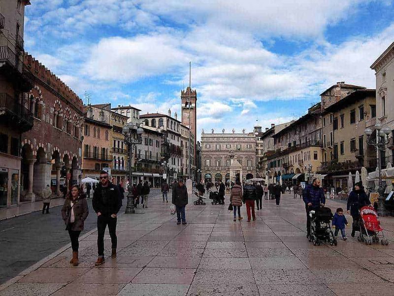 Verona, leggende dei quartieri medievali 15 Passeggiata camminando nel centro storico di Peschiera del Garda, con persone, negozi e architettura storica, cielo nuvoloso e atmosfera vivace.