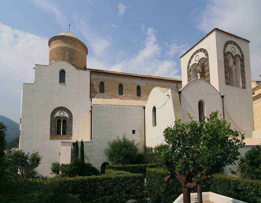 Bellissima chiesa storica in stile medievale con torri e pareti bianche, immersa in un giardino ben curato e highlighting l’architettura iconica, ideale per contenuti su turismo culturale e patrimonio storico.