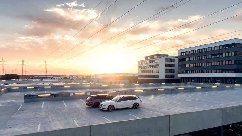 Poliurea, impermeabilizzazione a spruzzo dei parcheggi. Auto parcheggiata sul rooftop di un edificio moderno durante un tramonto, con cielo colorato e linee elettriche in background, rappresentando un esempio di parcheggio urbano e architettura innovativa.