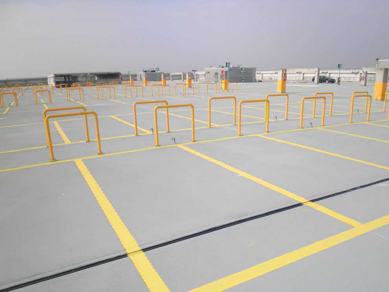 Poliurea, impermeabilizzazione a spruzzo dei parcheggi 4 Poliurea, impermeabilizzazione a spruzzo dei parcheggi. Parcheggio per auto in un grande parcheggio coperto con barriere di sicurezza gialle, spazio per diverse vetture, senza veicoli in sosta, in un'area moderna e ben segnalata.