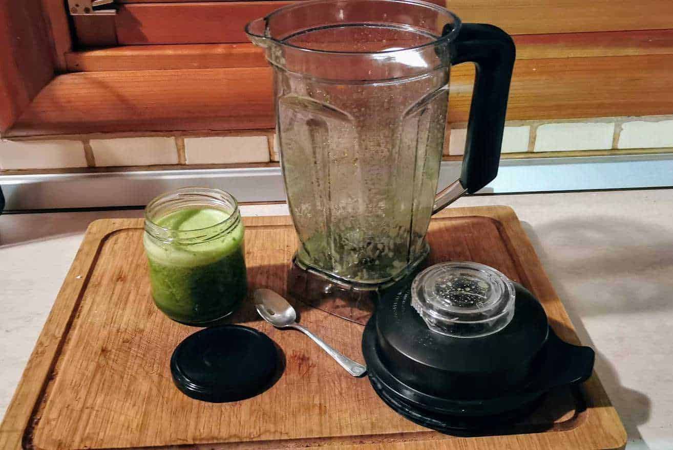 Frullatore con residui di verdura, barattolo di succo di cetriolo, e accessori su un tagliere di legno in cucina, ideali per preparare smoothies e detox.
