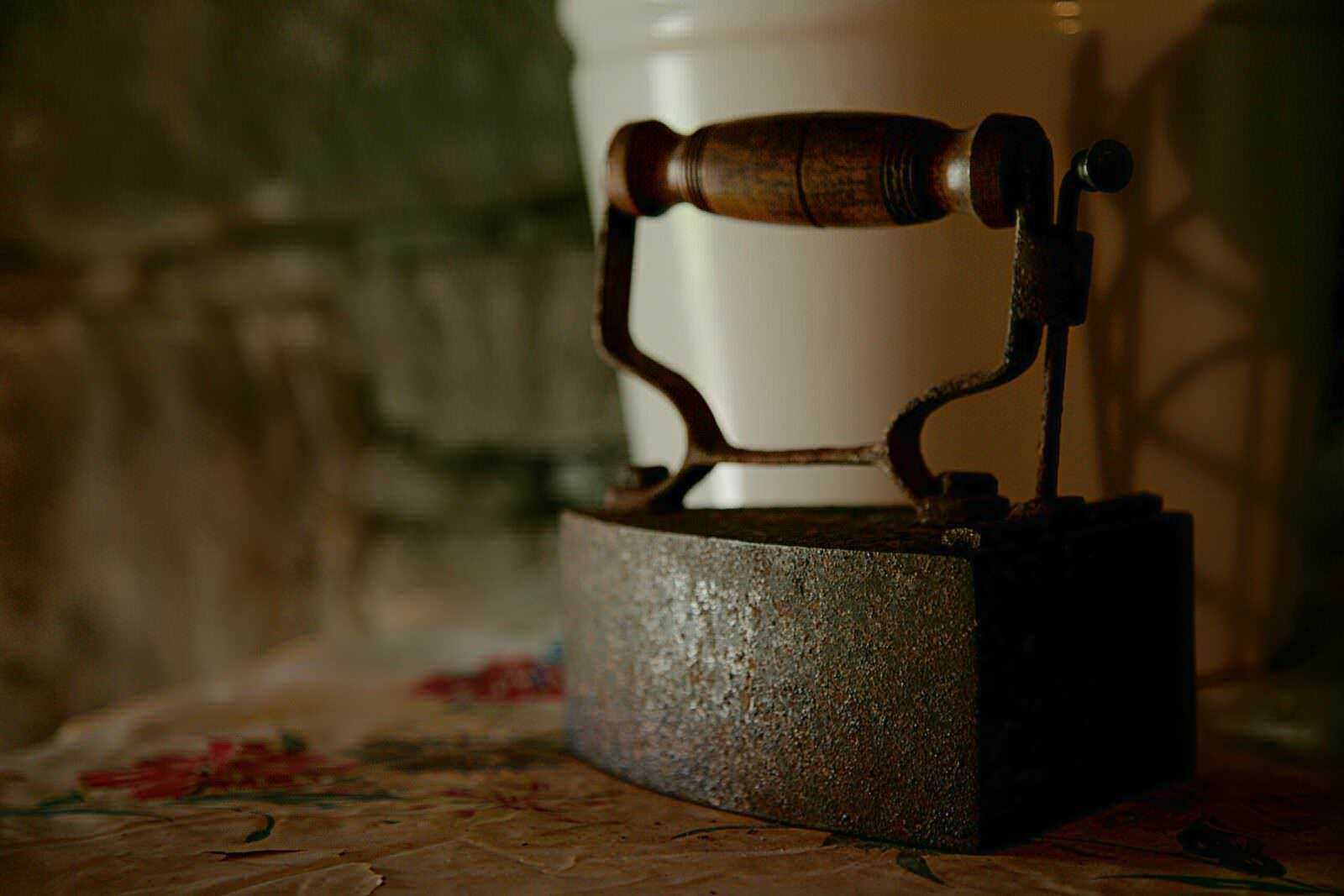 Più dettagliato: Antica piastra a vapore in ferro battuto con manico in legno, posizionata su una superficie di piastrelle decorative, ambiente rustico e vintage, perfetta per decorazioni di antiquariato o collezionismo.