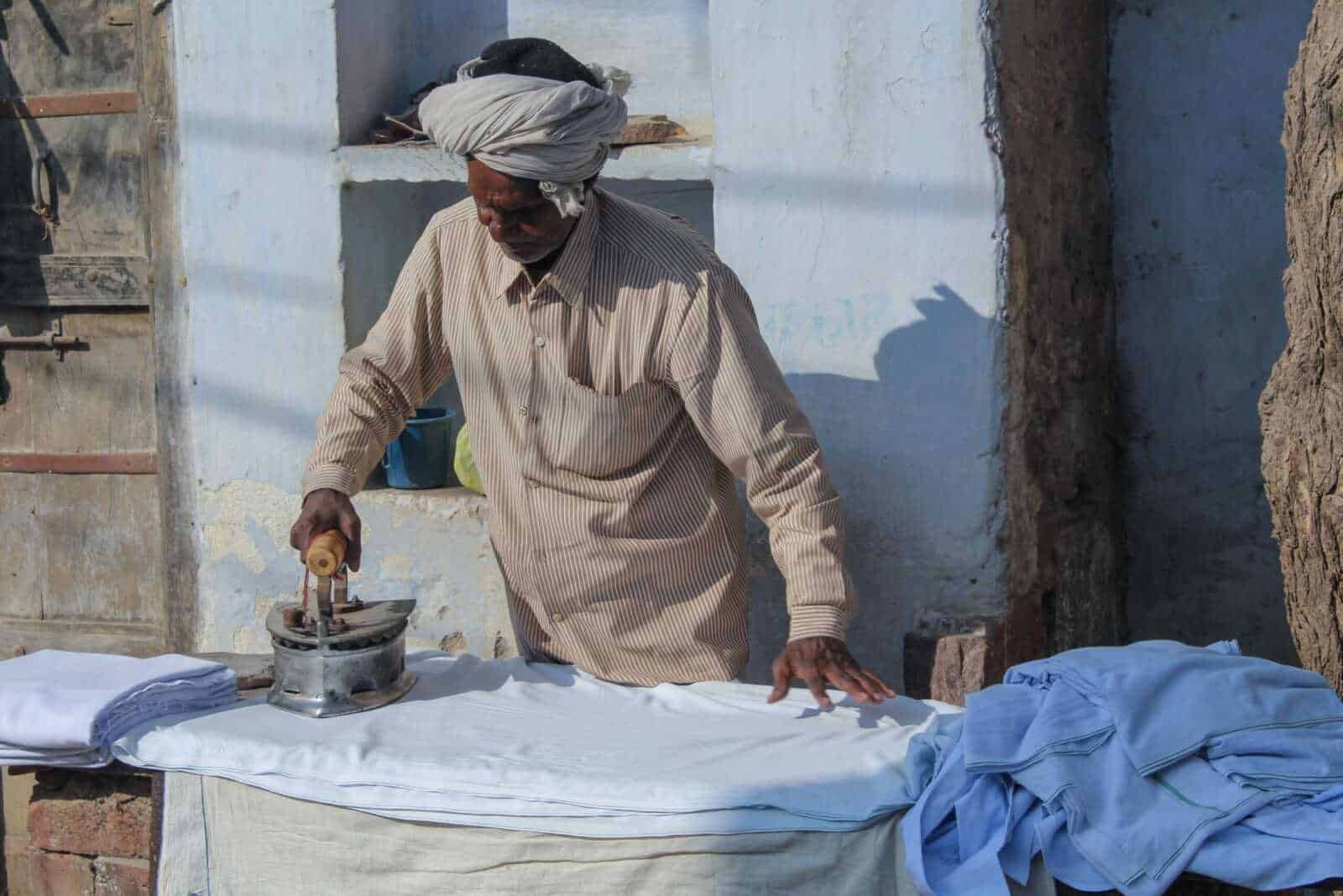 Fitto di un uomo africano che stira indumenti bianchi all'aperto con un ferro da stiro manuale, in un ambiente rustico e tradizionale.