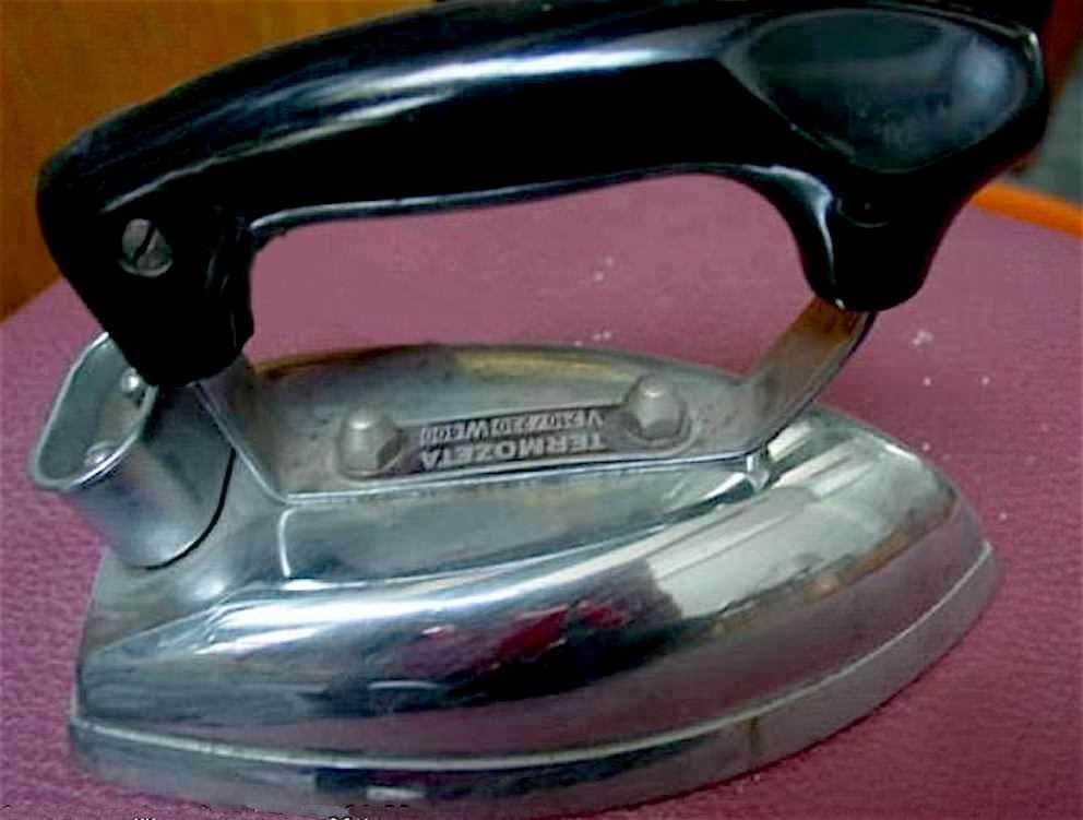 Ferro da stiro vintage in metallo e plastica, superficie liscia e ergonomica, oggetto domestico per stirare i vestiti, posizionato su un tavolo rivestito di tessuto rosso.