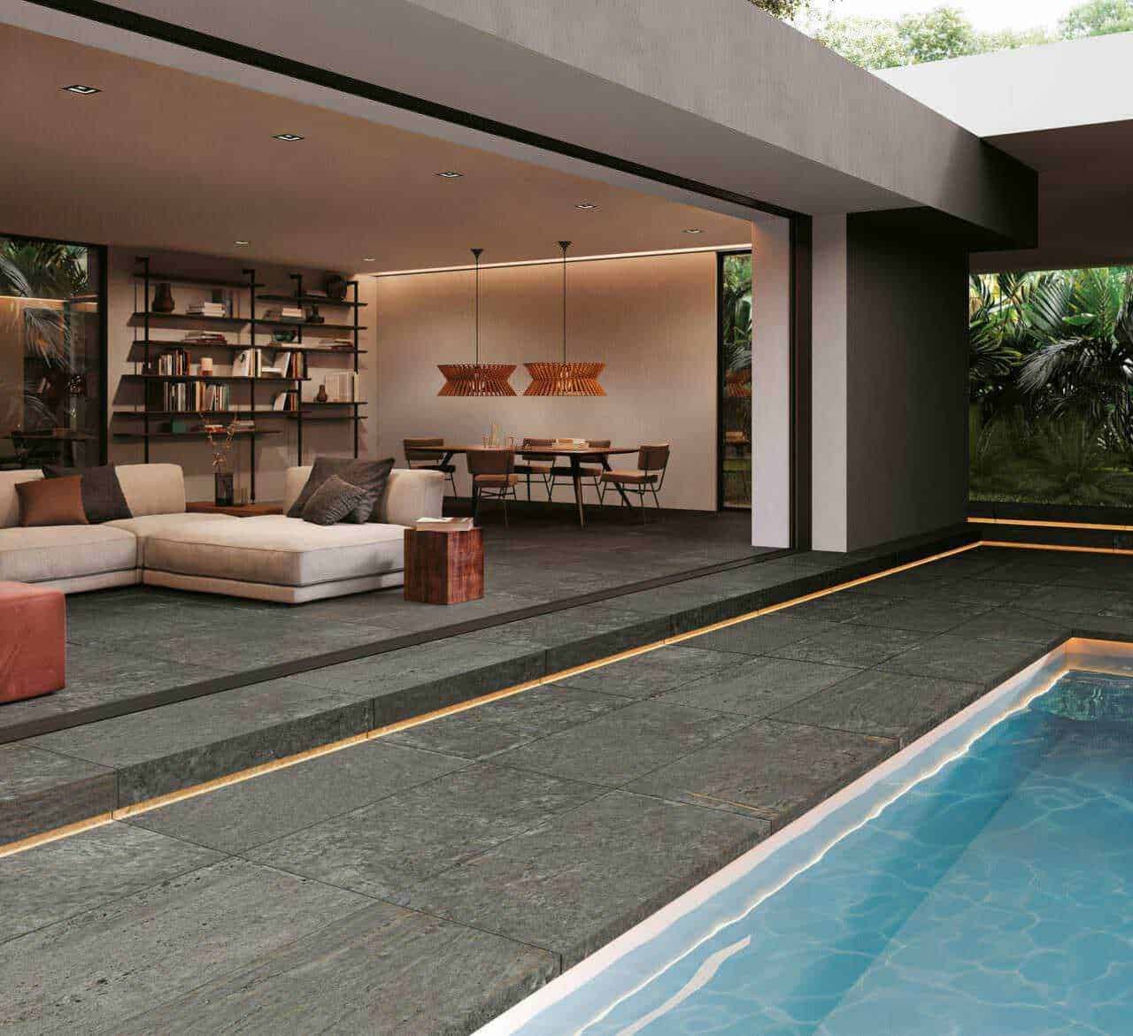Ampia zona living con divano beige e libreria moderna, spazi esterni con piscina e giardino tropicale, arredamento elegante e design contemporaneo, ideale per case di lusso e relax docce in piscina.