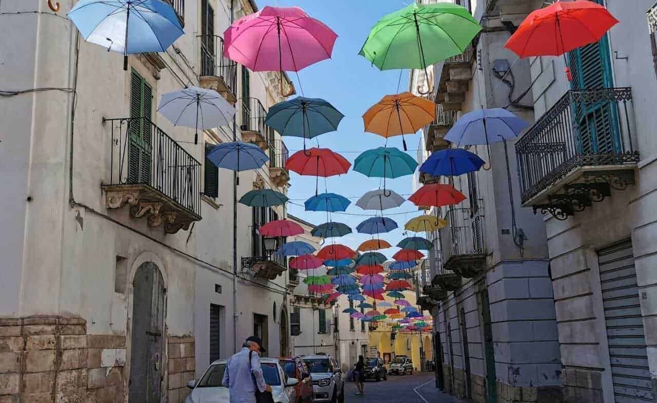 Colorati ombrelli appesi sopra strade di un quartiere storico, decorazione artistica e colorata creata per abbellire l'ambiente e attirare visitatori, perfetta per foto e giornate di sole.