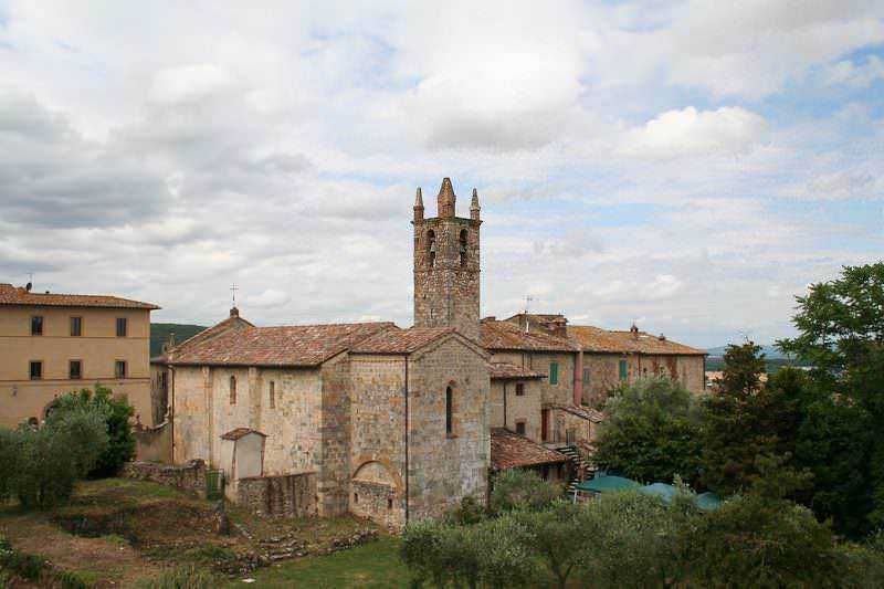 Antico borgo medievale con torre in mattoni, case in pietra e paesaggio toscano in background, ideale per appunti sul blog di viaggio e storia italiana.