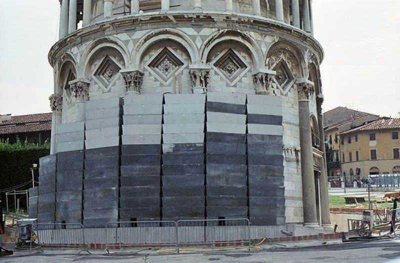 Immagine di lavori di restauro e conservazione sulla Torre Pendente di Pisa con protezioni in bambù e sostegni temporanei. Intervento di manutenzione sulla rinomata attrazione turistica italiana.