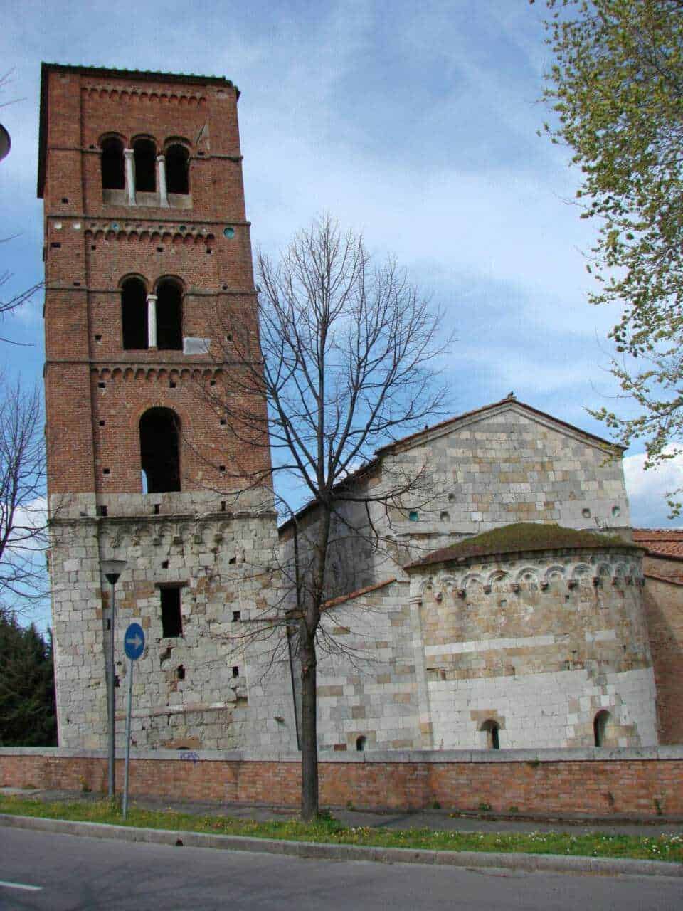 Torri medievali in mattoni rossi, chiesa antica con dettagli architettonici storici, paesaggio urbano con alberi e cielo sereno, architettura storica in Italia, foto di un monumento storico.
