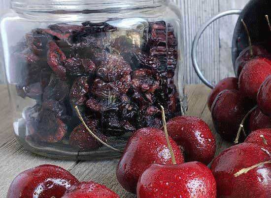 Fiocchi di ciliegie fresche e essiccate in barattolo di vetro con ciotola di ciliegie fresche intorno, simbolo di conserve di stagione e ricette dolci fatte in casa.