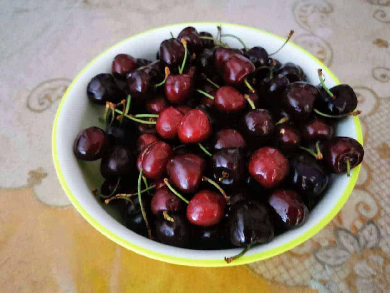 Mandorle ciliegie fresche in ciotola, frutta estiva, snack naturale e salutare, raccolto di stagione, alimenti ricchi di antiossidanti, dolce naturale, fonte di vitamine, con stelo verde, vivace e invitante.