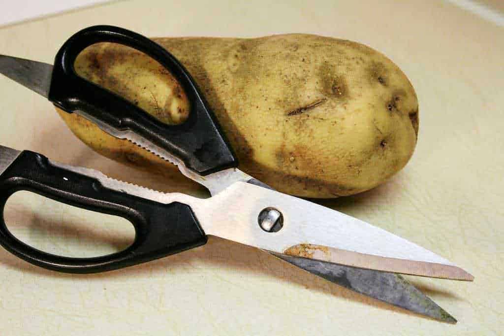 Scorza di patata con forbici da cucina su piano di lavoro pulito.