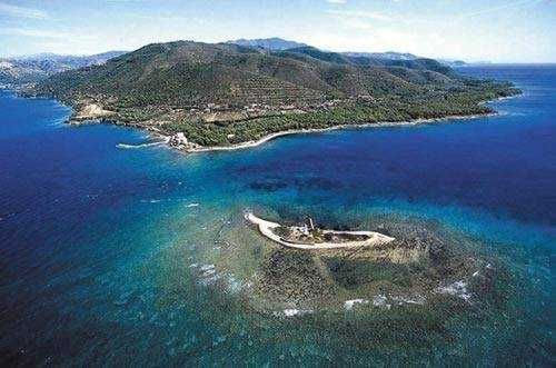 Vista aerea dell'isola e della costa mediterranea con acque cristalline e pineta, ideale per vacanze estive e relax in natura.