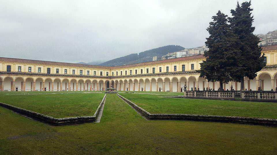 Elegante cortile storico con archi e verde ben curato, situato in un edificio di pregio in Italia, con sfondo montano e atmosfera mistica.