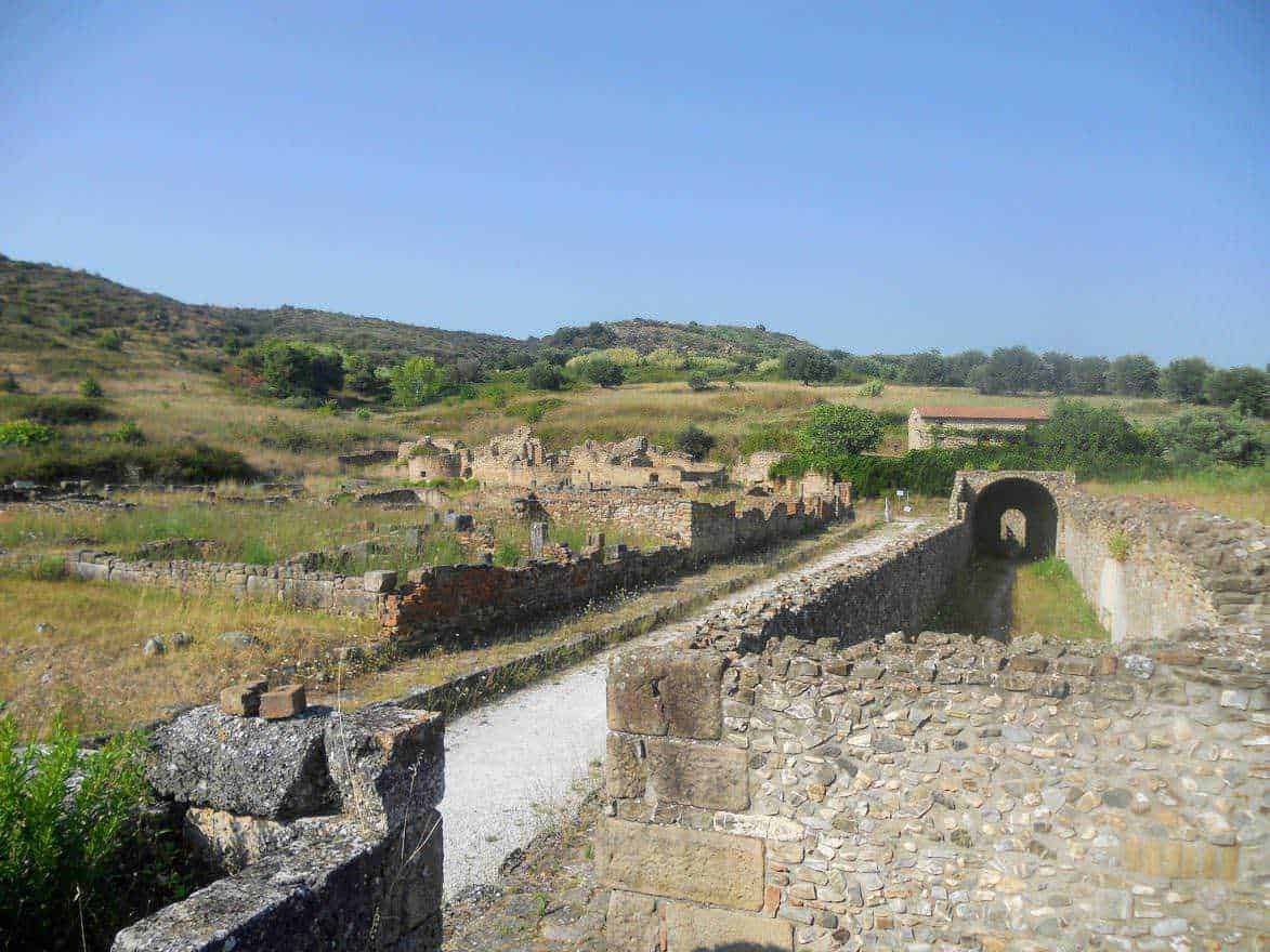 Antico sito archeologico di Roma antica con resti di mura e porte, immerso in un paesaggio collinare verde, ideale per appunti su storia e archeologia.