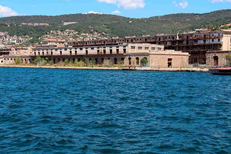 Trieste asburgica, 9 siti da raggiungere a piedi 10 Luminoso piazza storica con edifici in stile classico e bandiere italiane, sotto un cielo nuvoloso, zona centrale di una città italiana.