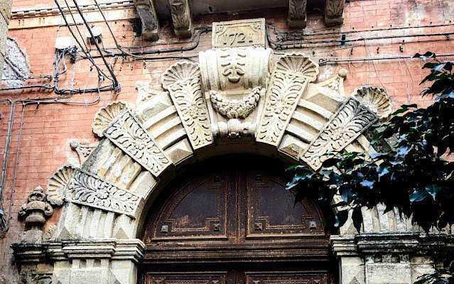 Antico portale in pietra con elementi decorativi in stile rinascimentale e arco in pietra, situato su un edificio storico in Italia. Muratura in mattoni visibile sullo sfondo con dettagli architettonici dettagliati.