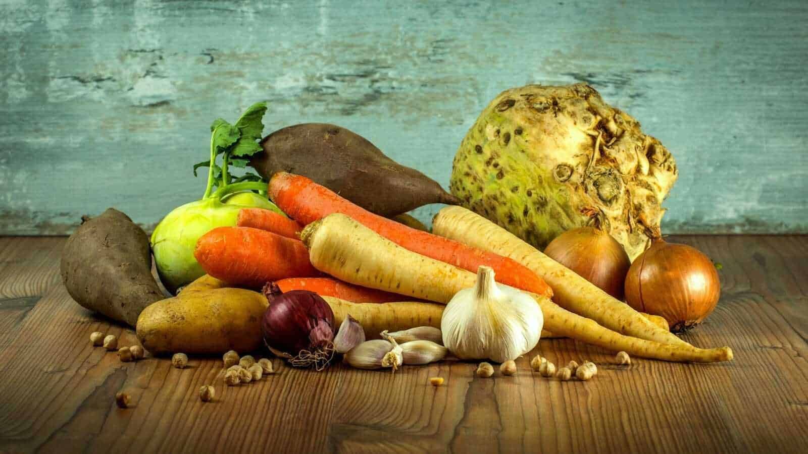 Verdure crude o cotte: Pomodori, cipolle, aglio, carote, patate e pastinaca su tavolo di legno, collezione di verdure organiche fresche e salutari.